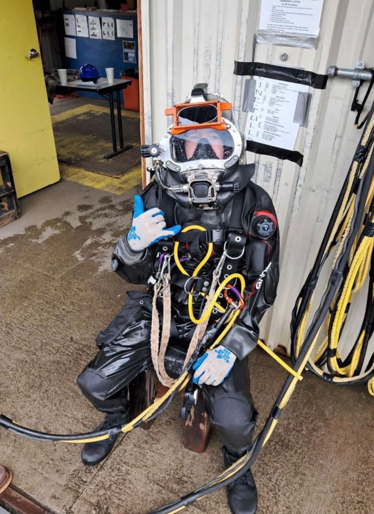 Diver in a sealed drysuit and helmet during a pre-dive check, with umbilical attached